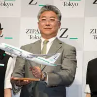 制服姿のモデルとともに機材の模型を掲げるZIPAIRの西田真吾社長