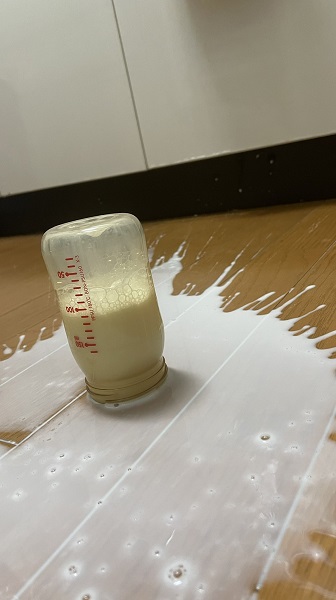 フタが外れた哺乳瓶が真っ逆さまに落ち、入っていたミルクが床に広がっている光景