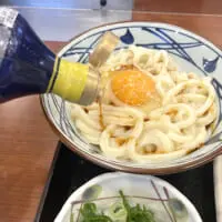 丸亀製麺の釜玉うどんと、だし醤油をかけていく